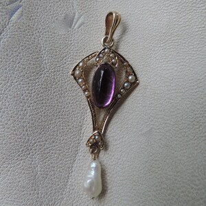 Puede incluir: Colgante de oro con una piedra amatista ovalada, rodeada de peque&ntilde;as perlas. Una perla en forma de l&aacute;grima cuelga de la parte inferior. El colgante tiene un dise&ntilde;o Art Nouveau ornamentado.