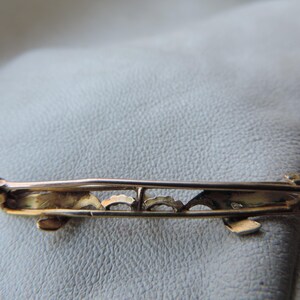 May include: A gold-toned brooch with a delicate, intricate design. The brooch has a pin and a safety catch on the back.