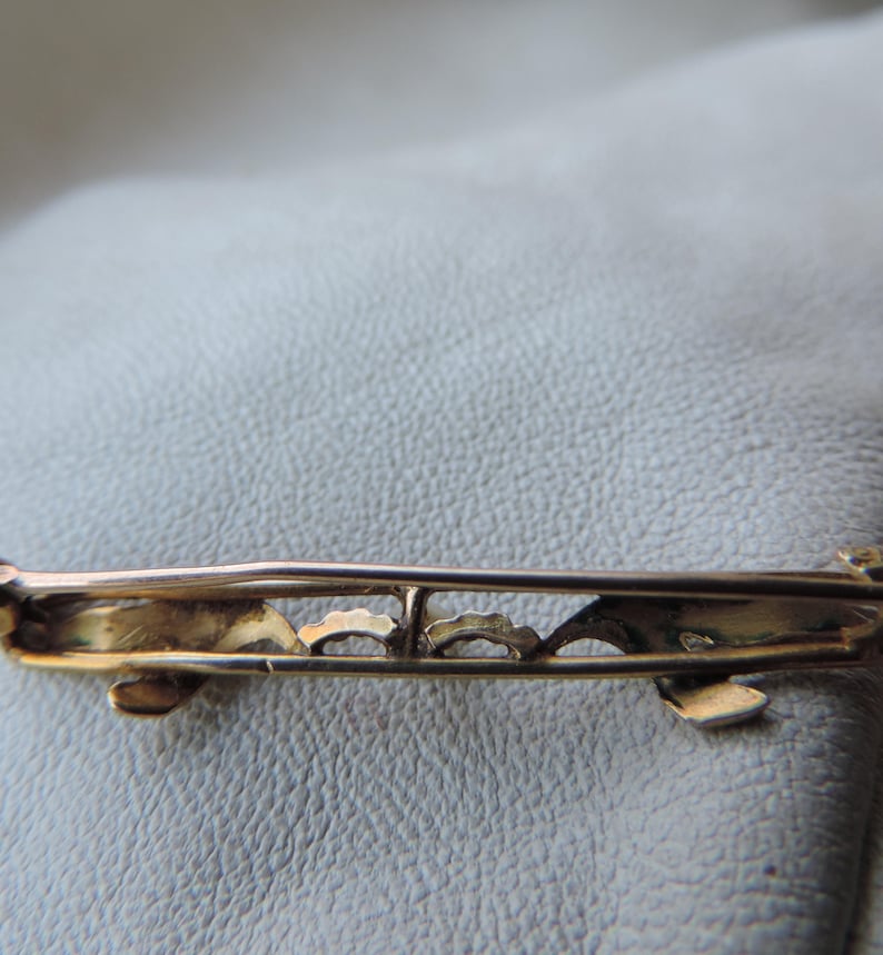 May include: A gold-toned brooch with a delicate, intricate design. The brooch has a pin and a safety catch on the back.