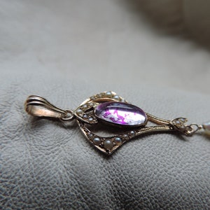 Puede incluir: Colgante dorado con una gran gema rosa ovalada en el centro. El colgante est&aacute; adornado con peque&ntilde;as perlas y detalles de filigrana intrincados. El dise&ntilde;o es ornamentado y de inspiraci&oacute;n vintage, con una delicada cadena.
