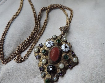 May include: A gold chain necklace with a pendant featuring a red stone surrounded by white, green, and purple stones.
