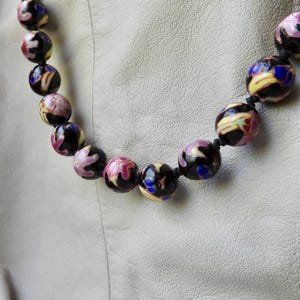 May include: A beaded necklace featuring large, round beads in shades of black, pink, yellow, and blue. The beads have a glossy finish and are strung on a black cord. The necklace is a statement piece.