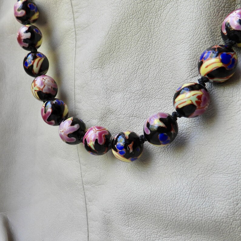 May include: A beaded necklace featuring large, round beads in shades of black, pink, yellow, and blue. The beads have a glossy finish and are strung on a black cord. The necklace is a statement piece.