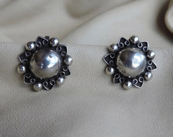 May include: A pair of silver earrings with a circular design. The earrings have a textured surface and a raised edge.