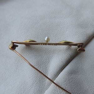 May include: A gold-toned brooch with three green stones and a single pearl in the center. The brooch has a pin and catch closure.