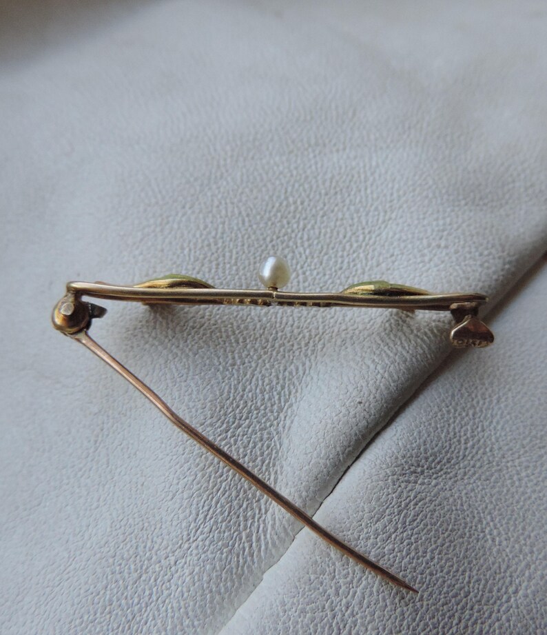 May include: A gold-toned brooch with three green stones and a single pearl in the center. The brooch has a pin and catch closure.
