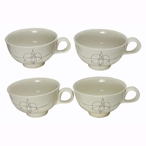 May include: A set of four off-white ceramic tea cups, each featuring a rounded handle and a base pedestal. The exterior of every cup is decorated with a thin, dark brown line drawing of an abstract, symmetrical, swirling geometric pattern.