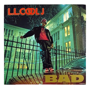 May include: Album cover for L.L. Cool J's "BAD" album. The cover features L.L. Cool J in a black leather jacket, red shirt, and red hat, leaning against a fence. The album title is in gold letters.