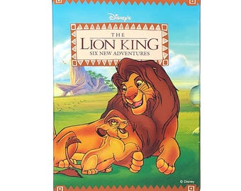 May include: A brown and orange box with a picture of Simba and Mufasa from Disney's The Lion King. The text on the box reads "Disney's The Lion King Six New Adventures".