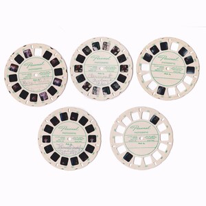 May include: Five circular off-white View-Master reels featuring Personal Photographs. Each reel contains seven rectangular film frames with various images. The center of each reel has green text reading Personal Photographs and Made By, with some handwritten notes.
