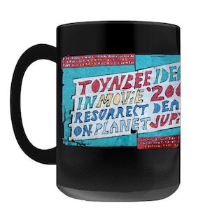 May include: Black ceramic mug with a black handle. The mug features a colorful design with the text "TOYNBEE IDEA IN MOVIE 2001 RESURRECT DEAD ON PLANET JUPITER" in various colors on a blue background.
