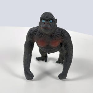 May include: A black gorilla figurine with blue eyes and a red chest. The gorilla is in a quadrupedal stance, with its arms and legs extended. The figurine is made of a textured material.