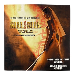 Puede incluir: Portada del CD de "Kill Bill Vol. 2" con una mujer vestida de novia sosteniendo una espada. La portada tiene un esquema de color cálido y dorado con el título de la película en letras en negrita y estilizadas. El texto incluye "The New Film by Quentin Tarantino" y fechas de lanzamiento.