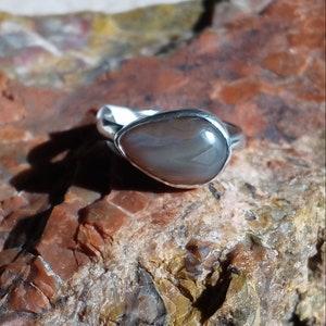 K&ouml;nnte beinhalten: Ein silberner Ring mit einem tropfenf&ouml;rmigen grauen Achat-Stein.