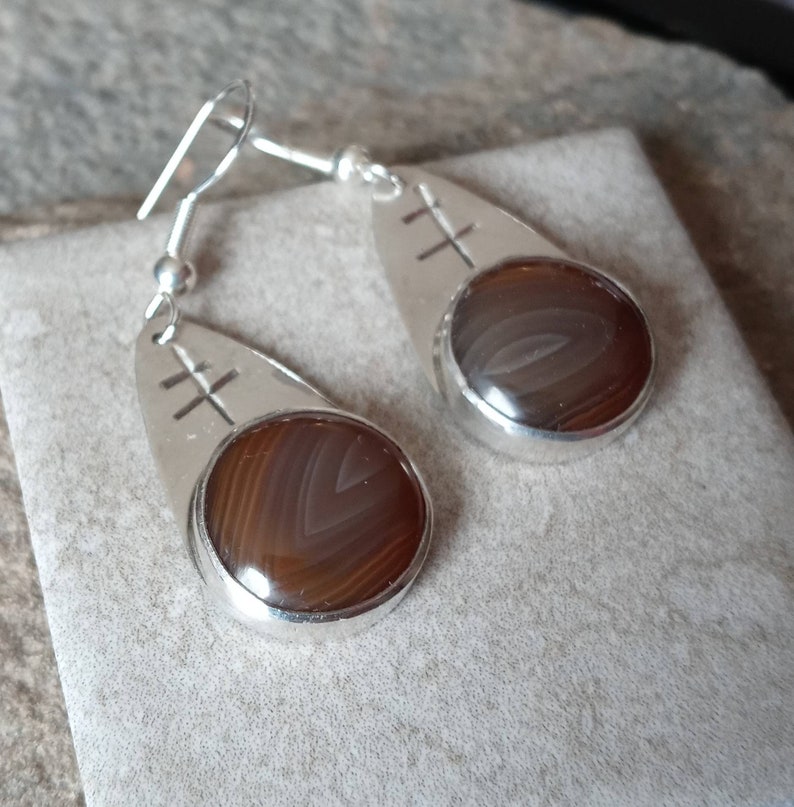 May include: A pair of silver dangle earrings with brown agate stones and a cross design.