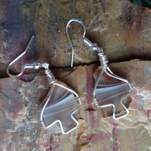 May include: A pair of silver wire wrapped earrings with brown and white agate stones. The stones are irregularly shaped and have a natural, organic look.