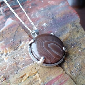 May include: A silver chain necklace with a brown agate pendant. The pendant is set in a silver bezel and has a swirling pattern.