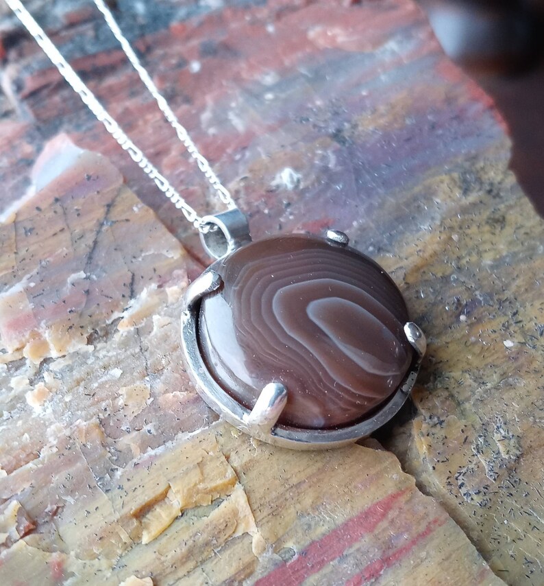 May include: A silver chain necklace with a brown agate pendant. The pendant is set in a silver bezel and has a swirling pattern.