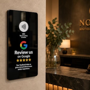 Könnte beinhalten: Ein rechteckiges schwarzes Schild an einer Wand mit einem NFC-Symbol, dem Google-Logo und dem Text Review us on Google sowie fünf gelben Sternen. Unter den Sternen steht der Text Your feedback helps us grow and provide an even better experience.