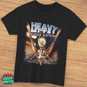 Könnte beinhalten: Schwarzes T-Shirt mit einem Grafikdruck einer Frau, die ein geflügeltes Wesen reitet. Die Grafik ist in Braun-, Orange- und Gelbtönen gehalten. Der Text "Heavy Metal" ist in silbernen Buchstaben über der Grafik gedruckt.