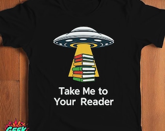 May include: A black t-shirt with a graphic of a flying saucer hovering over a stack of books. The text "Take Me to Your Reader" is printed below the graphic.