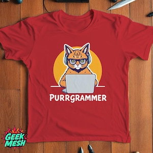 以下が含まれることがあります： ヘッドホンとメガネをかけた漫画の猫がラップトップで作業している赤いTシャツ。「PURRgrammer」の文字が猫の下にあります。シャツには「GEEK MESH」のロゴも付いています。