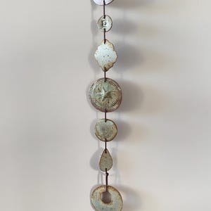 May include: A ceramic hanging mobile in shades of blue and brown, composed of various shapes connected by a dark cord. The design includes circles, a teardrop, and a starburst, offering a unique decorative element.