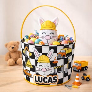 Könnte beinhalten: Ein Osterkorb mit gelbem Griff und Rand, mit einem schwarz-weißen Schachbrettmuster. Der Korb ist mit Bau-Grafiken und dem Namen "LUCAS" verziert. Er enthält ein Plüschkaninchen mit gelbem Helm und bunte Ostereier.