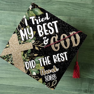 May include: Black graduation cap with gold glitter and green floral accents. The text "I Tried My Best & God Did The Rest" is written on the cap. The name "Hannah" and the year "2025" are also written on the cap.