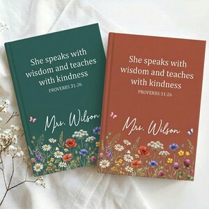 May include: Two hardcover journals, one teal and one rust-colored, with floral designs at the bottom. Each journal features the text "She speaks with wisdom and teaches with kindness PROVERBS 31:26" and the name "Mrs. Wilson".