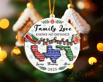 May include: A white Christmas ornament with the text "Family Love Knows No Distance." It features state outlines of California, Texas, and Florida, with names and the year 2025. The ornament is decorated with snowflakes and a string of lights.