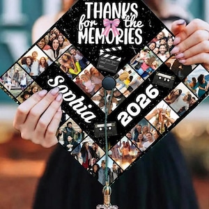 May include: Black graduation cap decorated with a collage of photos. The cap features the text "Thanks for the Memories" and "Sophia 2026" in white. A pink bow and film clapper are also visible. The cap is held by a person.