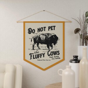 May include: A yellow and white banner with the text "Do Not Pet the Fluffy Cows" and a black and white illustration of a bison. The banner also includes the text "Think Safely Act Safely" and "National Park Service".