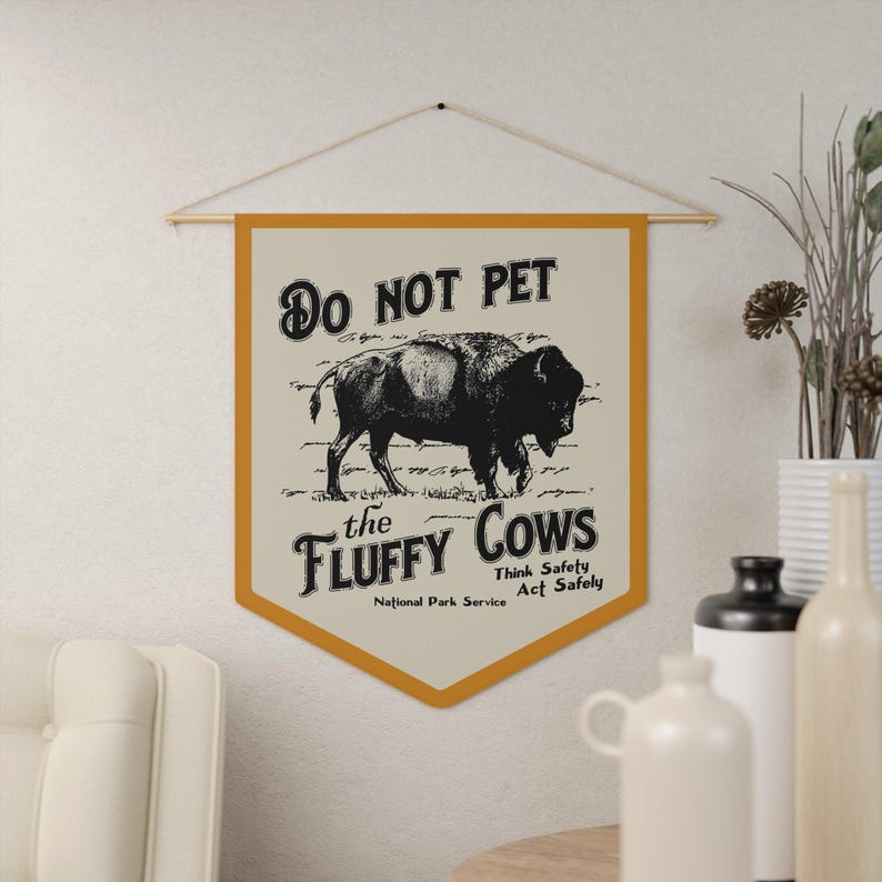 May include: A yellow and white banner with the text "Do Not Pet the Fluffy Cows" and a black and white illustration of a bison. The banner also includes the text "Think Safely Act Safely" and "National Park Service".