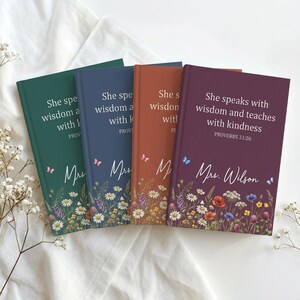 May include: Four hardcover journals in shades of green, blue, orange, and purple. Each journal features floral designs, butterflies, and text that reads "She speaks with wisdom and teaches with kindness" and "Mrs. Wilson."