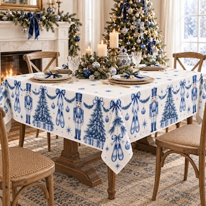 May include: A white tablecloth featuring a repeating blue pattern of nutcrackers, Christmas trees, bows, and ornaments. The fabric is draped over a wooden table, with the design printed across the surface in a festive, symmetrical arrangement.