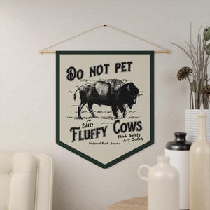 May include: A green and beige sign with the text "Do Not Pet the Fluffy Cows" and a black and white illustration of a bison. The sign also includes the text "Think Safely Act Safely" and "National Park Service".