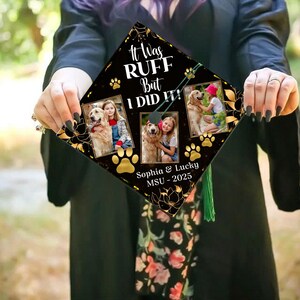 Può includere: Un cappello di laurea nero con accenti floreali dorati e impronte di zampe. Il cappello presenta tre foto incorniciate di una ragazza e un golden retriever. Il testo recita "It Was RUFF But I DID IT!" e "Sophia & Lucky MSU - 2025".