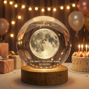 May include: A glass sphere featuring a detailed moon image, set on a wooden base. The sphere is inscribed with the name "Sophia" and the date "02.28.2010". The base reads "I love you!" with a heart. The scene is lit with warm lights.