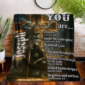 May include: A soft blanket with a lion's face, a knight, and the name "Joseph" in a decorative font. The blanket features the text "YOU are..." and inspirational phrases with Bible verses. The design uses a warm colour scheme of browns and golds.
