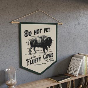 May include: A green and white sign with the text "DO NOT PET the FLUFFY COWS" and a black and white illustration of a bison. The sign also includes the text "Think Safety Act Safely" and "National Park Service".