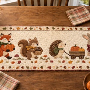 May include: A rectangular quilted table runner featuring an off-white background with a border of colorful autumn leaves and acorns. The center displays a fox, a squirrel, a hedgehog pulling a wooden cart, and a rabbit, all surrounded by mushrooms.