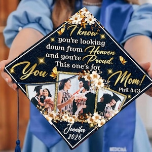 May include: A graduation cap with a dark blue background, gold accents, and floral decorations. The cap features the text "I know you're looking down from Heaven and you're Proud. This one's for Mom!" and includes photos. The name "Jennifer" and the year "2026" are also displayed.