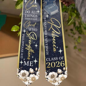 May include: Two navy blue graduation stoles with gold trim and floral accents. One stole reads "I can do all things through Christ who strengthens me" and the other reads "Rebecca Stanford University Class of 2026".