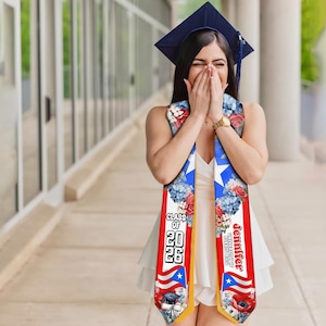 May include: A graduation sash with the Puerto Rican flag design, featuring red, white, and blue colors, floral accents, and the text "Class of 2026" and a name. The sash is worn over a white dress.