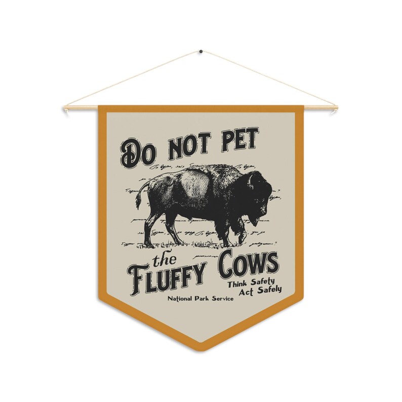 May include: A tan and orange pennant flag with the text "Do Not Pet the Fluffy Cows" and a black and white illustration of a bison. The text "Think Safety Act Safely" and "National Park Service" are also included.