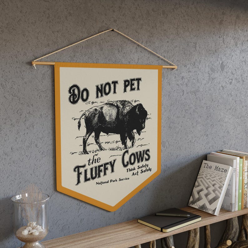 May include: A yellow and white sign with the text "DO NOT PET the FLUFFY COWS Think Safety Act Safely" and a black and white illustration of a bison. The sign is a National Park Service sign.