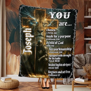 May include: A brown and gold blanket with a lion's face, a knight, and the text "YOU are..." with religious verses. The design includes a cross and lightning bolts. The name "Joseph" is also displayed on the blanket.
