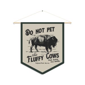 May include: A tan and green pennant with the text "Do Not Pet the Fluffy Cows" and a black and white illustration of a bison. The text "Think Safety Act Safely" is below the illustration. The text "National Park Service" is below the safety text.