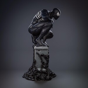 May include: Black and white statue of a superhero in a crouching pose, standing on a stone base with black vines. The superhero has a black suit with white webbing and a black mask with white eyes.